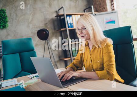 Foto di un allegro broker di occhiali vestiti che chattano un moderno gadget in casa workstation loft Foto Stock