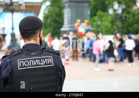 Un agente di polizia russo non identificato osserva attentamente la folla di persone nel centro di Mosca. Testo in russo: Polizia Foto Stock