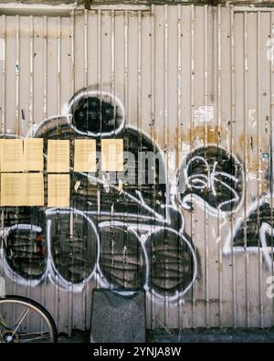 Art Urban Graffiti su muro in metallo industriale con avvisi gialli e dettagli a catena, che riflettono l'estetica urbana e la cultura di strada. Foto Stock