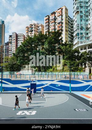 Vivace campo da pallacanestro urbano con bambini che giocano, incorniciato da alti edifici residenziali e alberi lussureggianti a Hong Kong Foto Stock