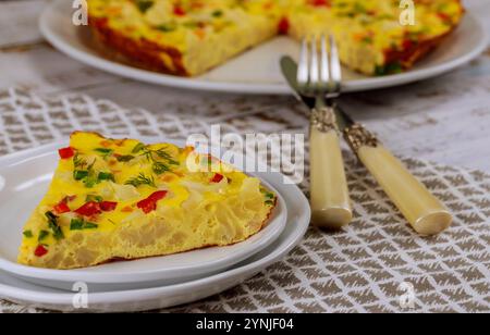 La gustosa frittata di verdure servita su piatto con forchetta e coltello presenta colori vivaci e ingredienti freschi Foto Stock