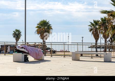 Civitavecchia, Italia - 13 novembre 2024: Una persona dorme su una panchina in una piazza vicino al lungomare Foto Stock