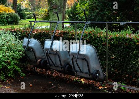 Tre carriole sono appese su una cremagliera circondata da vegetazione lussureggiante e foglie cadute. La tranquilla atmosfera del giardino mostra la bellezza della natura. Foto Stock