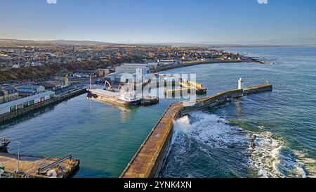 Buckie Harbour Moray Coast Scozia grande nave ormeggiata, faro e muro frangiflutti con onde e spruzzi Foto Stock