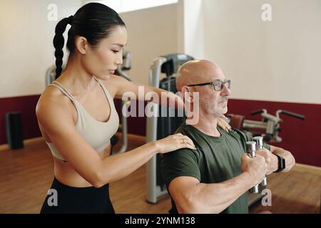 Assistenza all'uomo anziano per il sollevamento di pesi in palestra Foto Stock