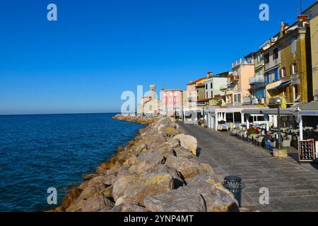 Pirano, Slovenia - 16 novembre 2024: Via ed edifici sulla costa adriatica con un faro alla fine nella città di Pirano in Istria Foto Stock