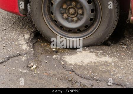 Un veicolo è immobilizzato a causa di uno pneumatico sgonfio, con la ruota appoggiata in un'ampia cavità su una superficie asfaltata, evidenziando la necessità della strada Foto Stock