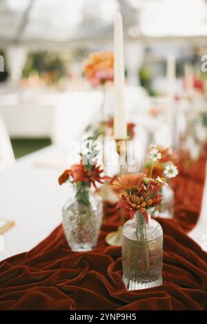 Elegante arredamento da tavolo sul retro con vivaci composizioni floreali autunnali, portacandele in ottone e un ricco portabandele in velluto di terracotta. Foto Stock