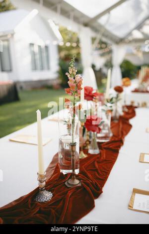 Elegante arredamento da tavolo sul retro con vivaci composizioni floreali autunnali, portacandele in ottone e un ricco portabandele in velluto di terracotta. Foto Stock