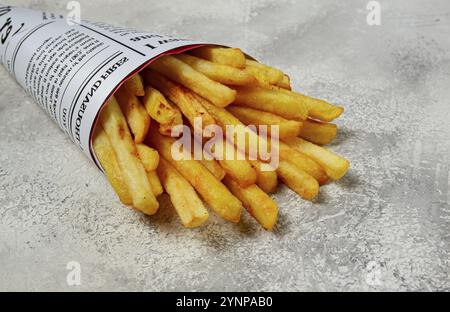 Fritte patatine fritte in un sacchetto di carta, su uno sfondo astratto, senza persone, in stile rustico, in una confezione conica, un giornale, una borsa del giornale Foto Stock