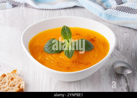 Cremosa zuppa di zucca guarnita con menta fresca servita in una ciotola bianca su un tavolo di legno Foto Stock