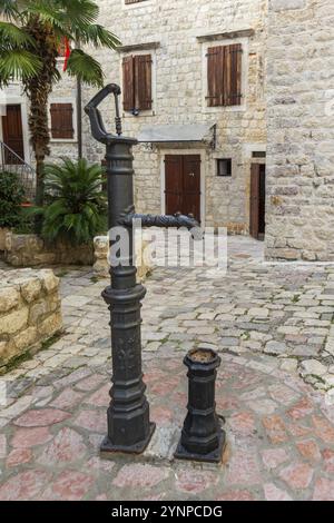 La vecchia colonna d'acqua con rubinetto si trova nel cortile di un edificio in pietra, Cattaro, Montenegro, Europa Foto Stock