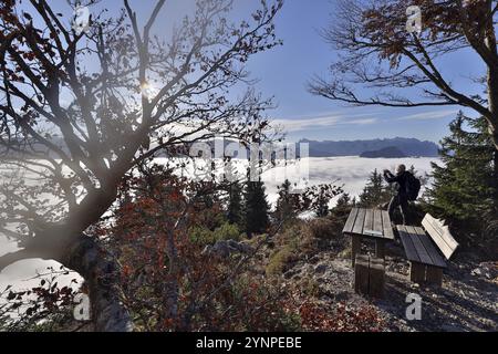 Un escursionista scatta una foto delle montagne che sorgono da un luogo di riposo con panchina e tavolo in legno, sole mattutino, Hochstaufen, alta Baviera, Baviera, Germania Foto Stock