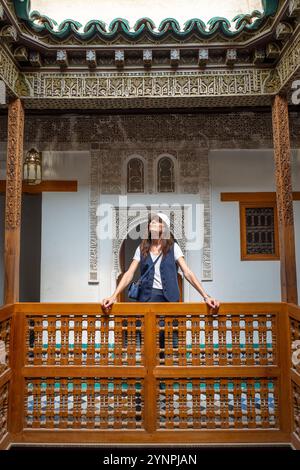 Giovane donna dai capelli scuri appoggiata su ringhiere di legno nel cortile della Madrasa di Ben Youssef, Marocco Foto Stock