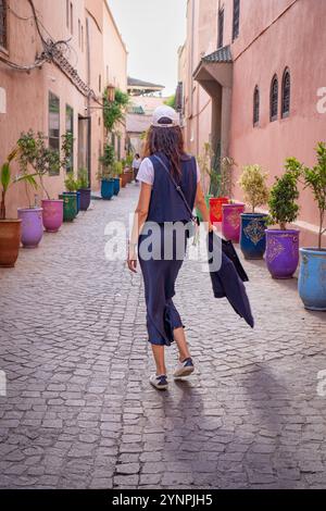 Giovane donna dai capelli scuri che cammina nelle strade rosse di Marrakech circondata da vasi colorati, il Marocco Foto Stock