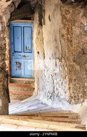 Porta blu intemprata adagiata in un antico muro di pietra con scale di mattoni al tramonto. Mentone, Provenza. Francia Foto Stock