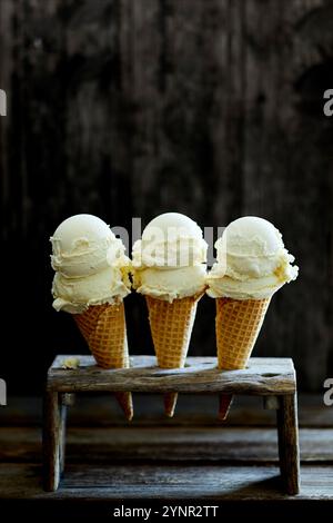 tre coni di gelato ripieni di gelato alla vaniglia in un gelato di legno su uno sfondo di legno scuro Foto Stock
