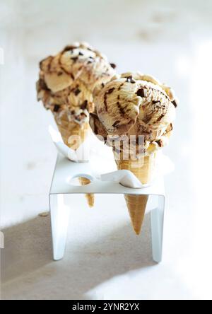 due coni di gelato ripieni di gelato alla banana split in un supporto di gelato bianco su sfondo beige Foto Stock