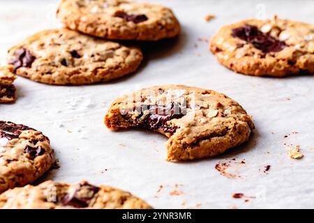 Un assortimento di biscotti appena sfornati con pezzi di cioccolato, alcuni sono stati parzialmente mangiati, appoggiati su carta pergamena. Foto Stock