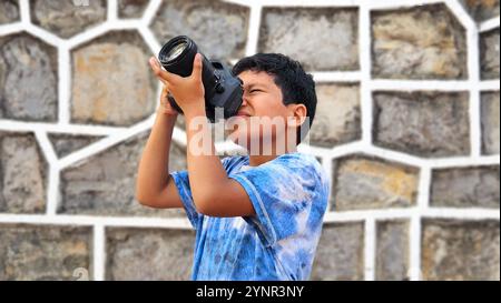 Un ragazzo latino di 10 anni dalla pelle scura impara a usare una macchina fotografica professionale, sogna e immagina di lavorare da adulto Foto Stock