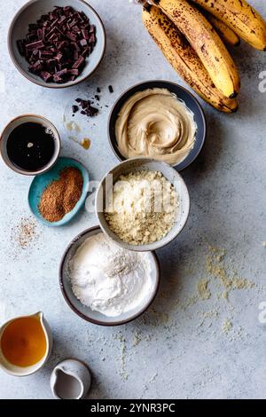 Un assortimento di ingredienti da forno, tra cui banane, cioccolato e polveri varie, disposti su un bancone della cucina. Foto Stock