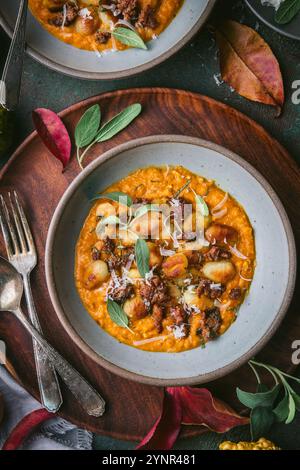 Un colpo ravvicinato di una ciotola di gnocchi croccanti in salsa di zucca con salvia e salsiccia disposti su una superficie verde scuro. Circondato da decorazioni autunnali, incluso Foto Stock