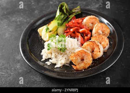 Gamberetti fritti e verdure come bok choy e peperoni rossi con riso, serviti su un piatto nero e ardesia scura, sano pasto fatto in casa in Asia st Foto Stock