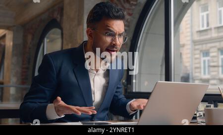 Stressato folle arrabbiato uomo arabo indiano uomo d'affari uomo uomo uomo d'affari uomo uomo uomo d'affari capo di affari che parla videochiamata in conferenza online computer portatile in ufficio Foto Stock