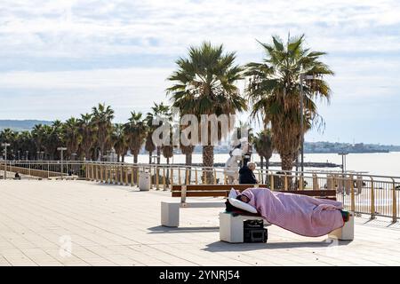 Civitavecchia, Italia - 13 novembre 2024: Una persona dorme su una panchina in una piazza vicino al lungomare Foto Stock
