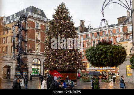 Londra, Regno Unito - 24 novembre 2024. Albero decorato a Natale, decorazioni al Covent Garden. Persone che camminano con gli ombrelli sotto la pioggia. Foto Stock