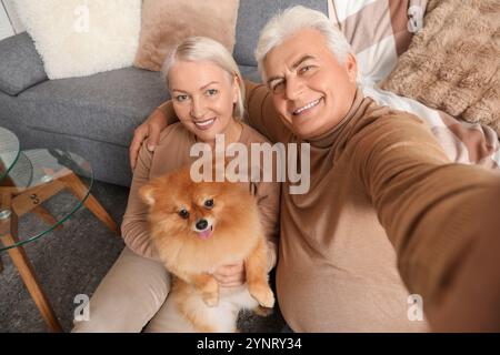 Felice coppia anziana con un carino cane della Pomerania che si fa selfie a casa Foto Stock