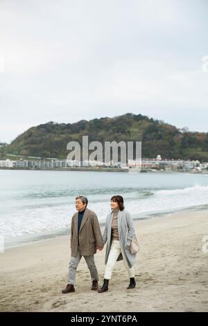 Uomo e donna che camminano lungo la spiaggia tenendosi per mano Foto Stock
