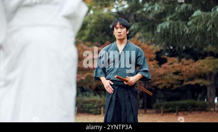 Spada, arti marziali e uomo in allenamento all'aperto con cultura, lotta coaching o sfida samurai nel parco. Armi di legno, guerrieri e giapponesi Foto Stock