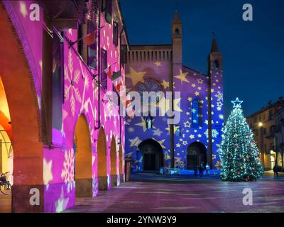 Storica chiesa italiana illuminata da proiezioni di luci colorate e decorata con albero di Natale nel centro della piazza acciottolata di Alba. Foto Stock