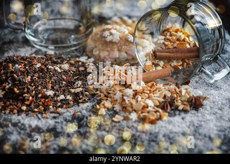 l'ingrediente invernale della bevanda calda, versato con spezie, zucchero a forma di stella e tazza di vetro, si capovolge su sfondo innevato e luci di sfocatura dorate Foto Stock
