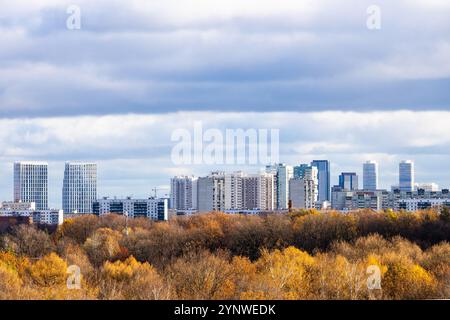 basse nuvole grigie blu sopra il colorato parco cittadino e gli appartamenti all'orizzonte il giorno d'autunno Foto Stock