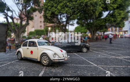 Un taxi bianco in miniatura si trova in cima alla piazza di Taxco de Alarcon, in Messico. Le strade acciottolate sono animate da gente del posto che si occupa di Foto Stock