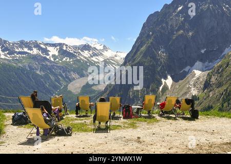 Vista posteriore degli escursionisti su sedie a sdraio presso la stazione della funivia Skyway Monte bianco, ammirando la vista della Val Veny e del Ghiacciaio Brenva in estate, Courmayeur Foto Stock