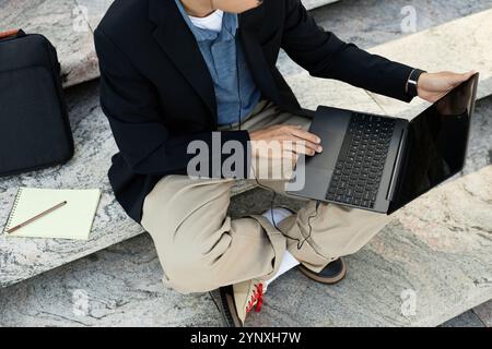 Immagine ritagliata di un programmatore IT irriconoscibile che utilizza un computer portatile per lavorare tenendo le dita sul touchpad mentre scrivi il codice su gradini di cemento all'esterno Foto Stock