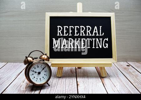 Testo di referral marketing scritto su lavagna con sveglia su sfondo in legno Foto Stock