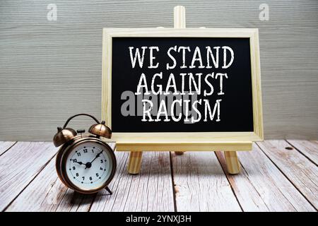 Testo We Stand Against Racism scritto su lavagna con sveglia su sfondo di legno Foto Stock