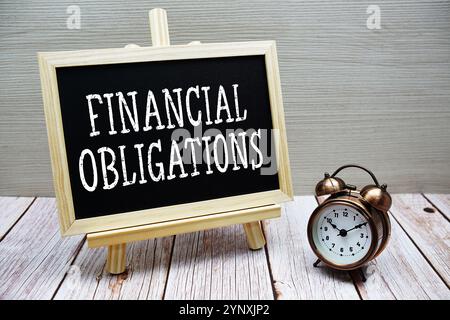 Testo degli obblighi finanziari scritto su lavagna con sveglia su fondo in legno Foto Stock