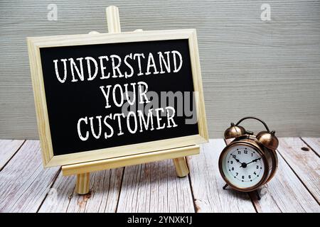 Comprendere il testo del cliente scritto sulla lavagna con sveglia su sfondo di legno Foto Stock