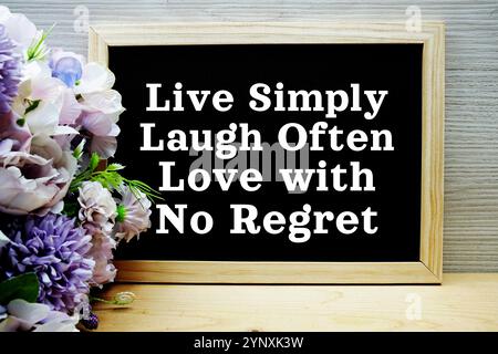 Vivi semplicemente ridi spesso ama senza rimpianti testo sulla lavagna con decorazioni con bouquet di fiori su sfondo in legno Foto Stock