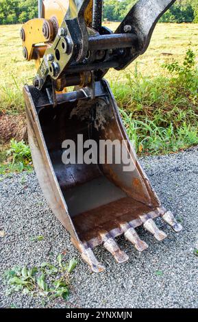 Uno sguardo ravvicinato di una pala della benna del retroescavatore parcheggiata su una strada dopo una tempesta. Un po' di acqua piovana sporca può essere visto all'interno della grande meccanica Foto Stock