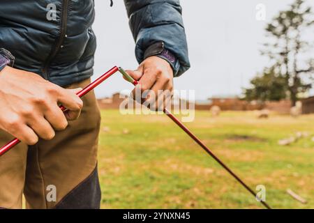 Le mani dell'uomo sistemano una tenda arancione sull'erba verde illuminata dalla luce naturale nella catena montuosa delle Ande Foto Stock