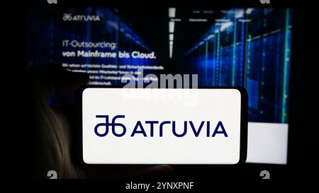 In questa immagine, una persona ha in mano uno smartphone con il logo dell'azienda tedesca di tecnologia dell'informazione Atruvia AG davanti alla pagina Web aziendale. Foto Stock