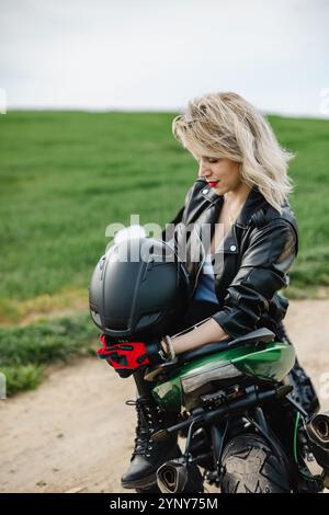 Donna con casco nero in pelle. Donna con una giacca in pelle nera che regge un casco nero, trasudando un look sicuro ed elegante. Perfetto Foto Stock