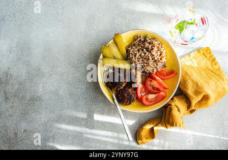 Vista dall'alto di grano saraceno, cotolette di carne, pomodori e cetriolini sottaceto con un bicchiere di acqua ghiacciata e menta fresca Foto Stock