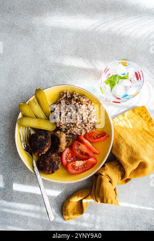 Vista dall'alto di grano saraceno, cotolette di carne, pomodori e cetriolini sottaceto con un bicchiere di acqua ghiacciata e menta fresca Foto Stock
